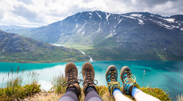 To turgåere tar en pause med utsikt over turkist fjellvann på fjelltur i Norge