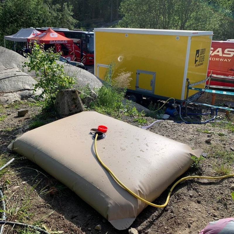 Vanntank i bruk på stevne for dusjformål; med hageslange for påfylling 